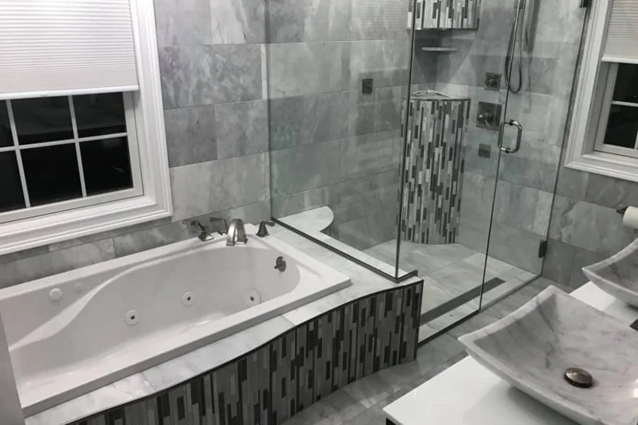 Gray tile bathroom with soaking tub, frameless glass shower enclosure, and mosaic accent tiles